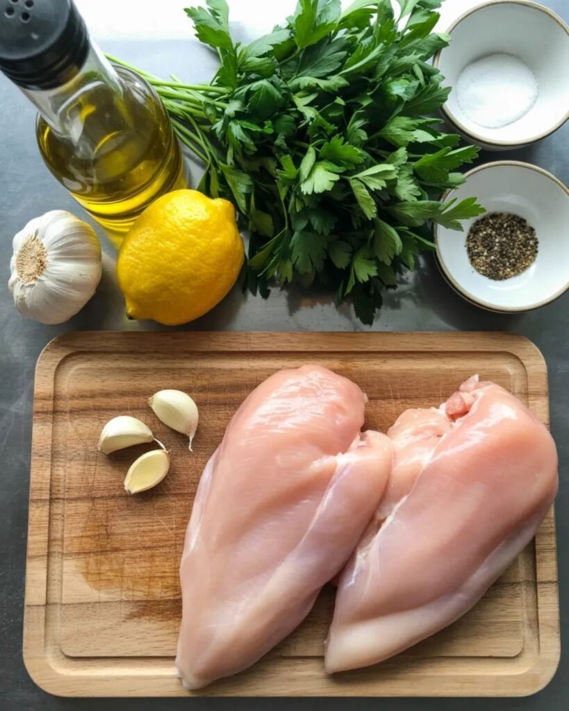 Ingredients for lemon garlic chicken including chicken breasts, lemon, garlic, and olive oil