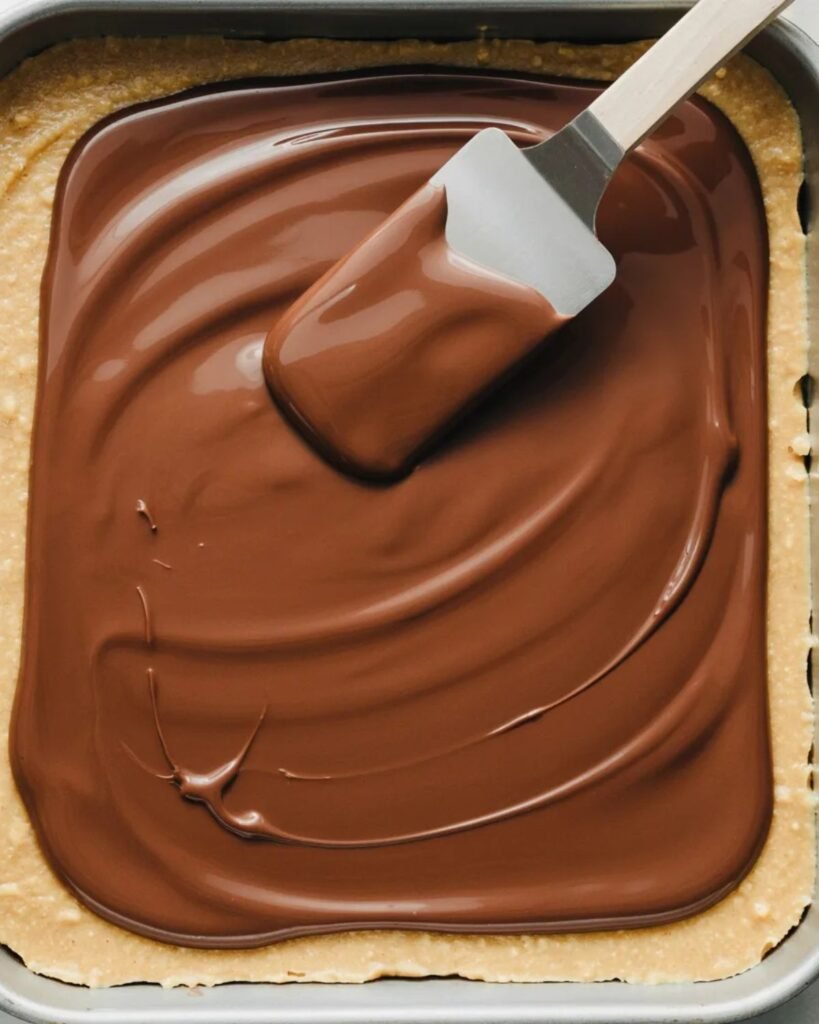 spreading chocolate topping over peanut butter bars in pan