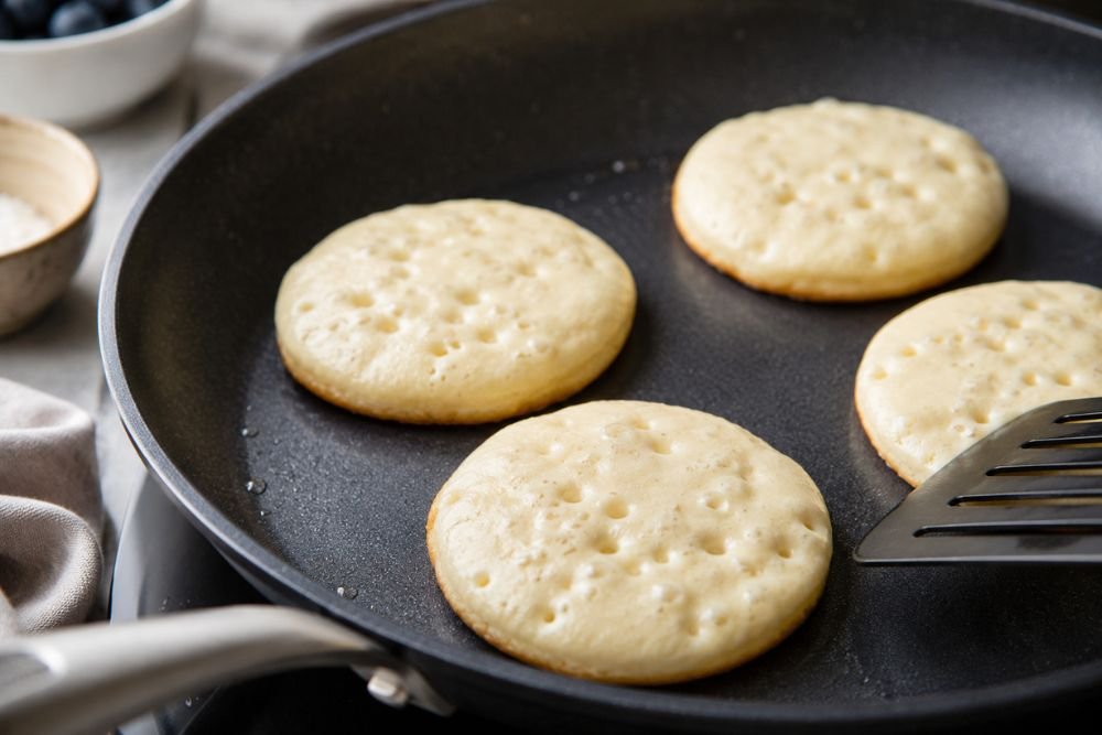 Small pancakes cooking on a skillet with bubbles and golden edges